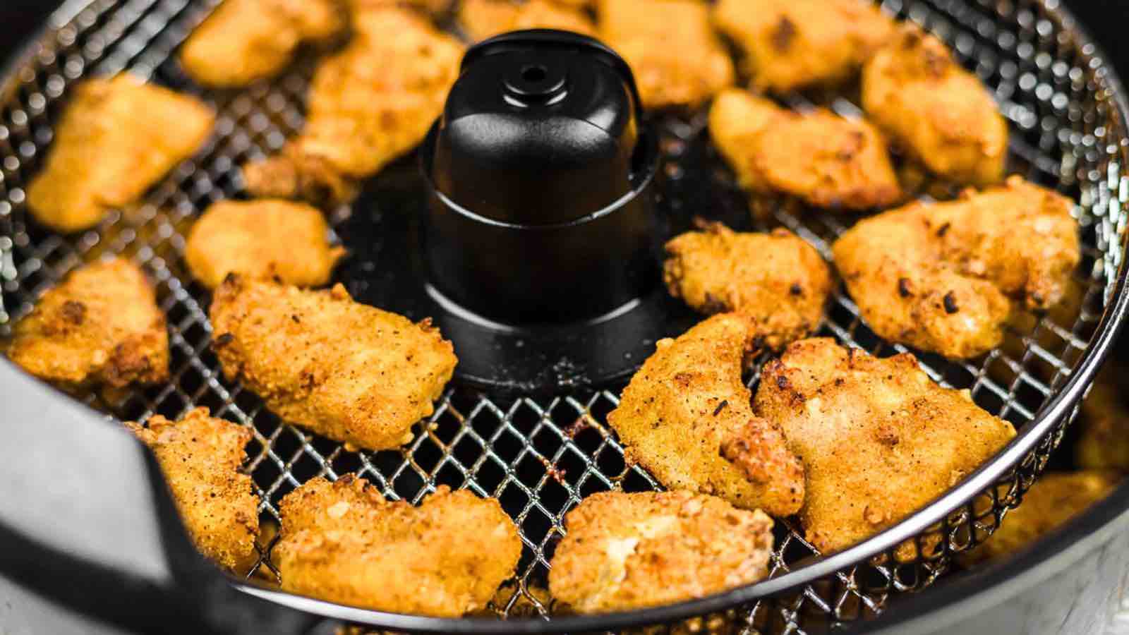 Air fryer basket filled with breaded chicken pieces cooking evenly.