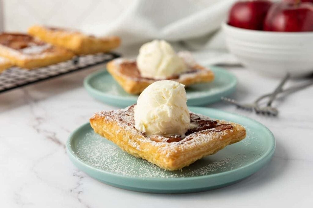 Two Upside-Down Apple Tarts topped with a scoop of vanilla ice cream and dusted with powdered sugar.