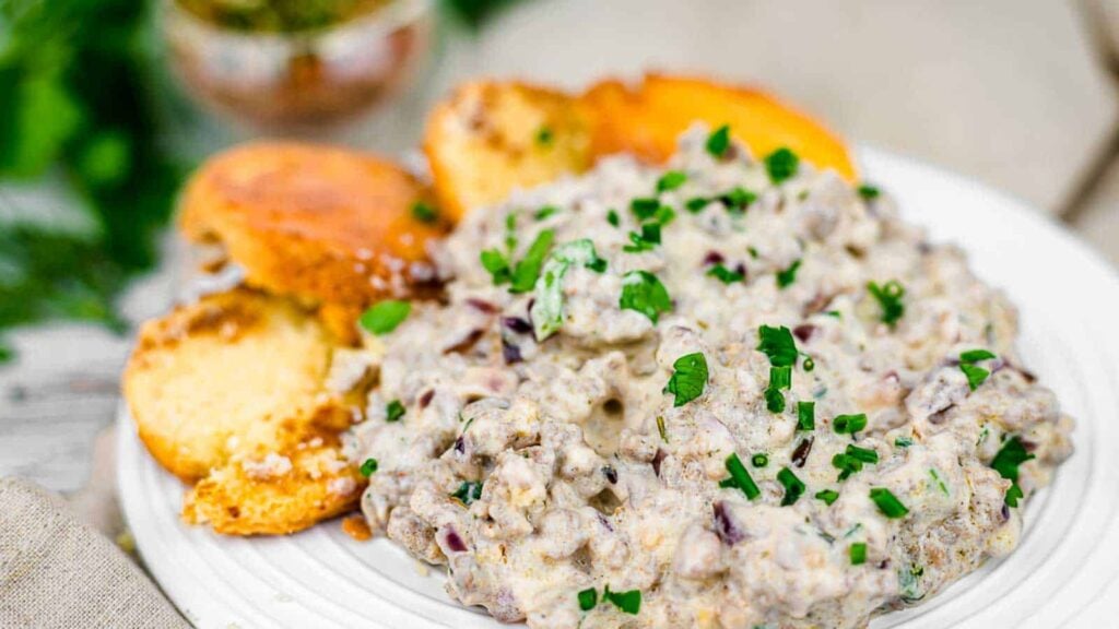 A plate of sausage gravy topped with chopped chives, served with slices of toasted bread on the side.