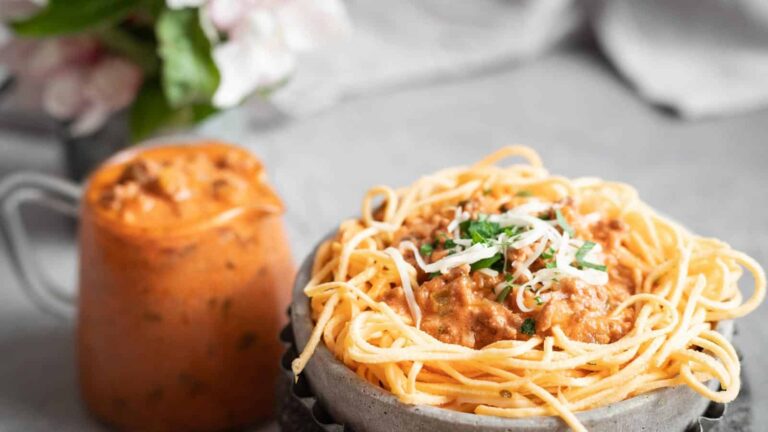 A bowl of spaghetti topped with meat sauce and grated cheese sits next to a jug filled with additional meat sauce.