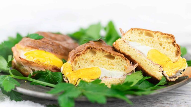 A plate with two breakfast sandwiches cut in half, showing egg, cheese, and ham inside, garnished with fresh parsley.