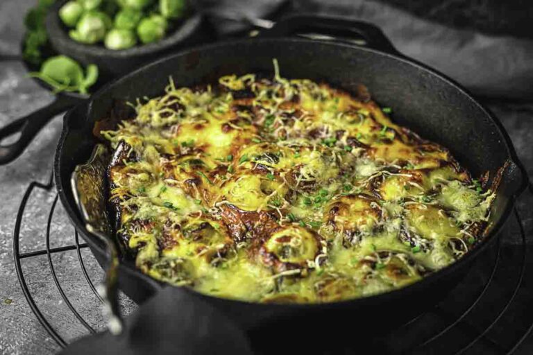 A cast iron skillet filled with baked Brussels sprouts topped with melted cheese and herbs, sitting on a wire rack.