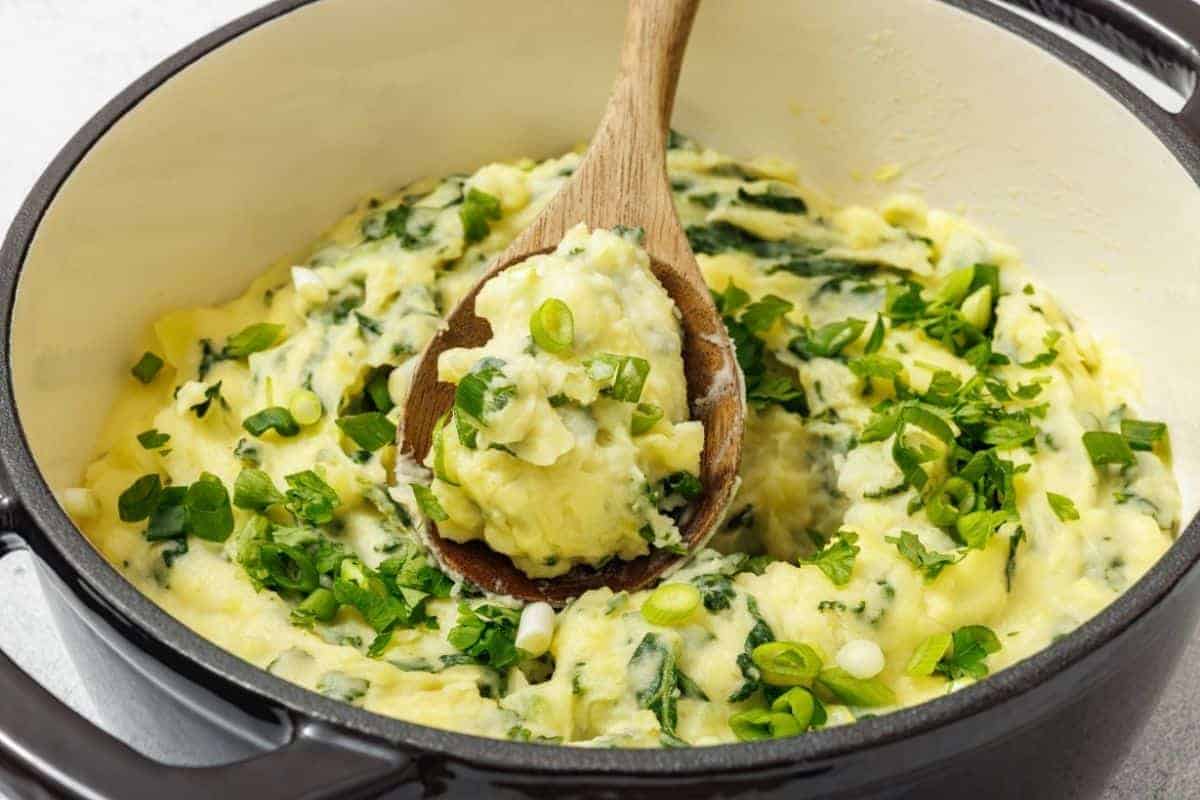A pot of Colcannon with Kale, with a wooden spoon lifting a portion.