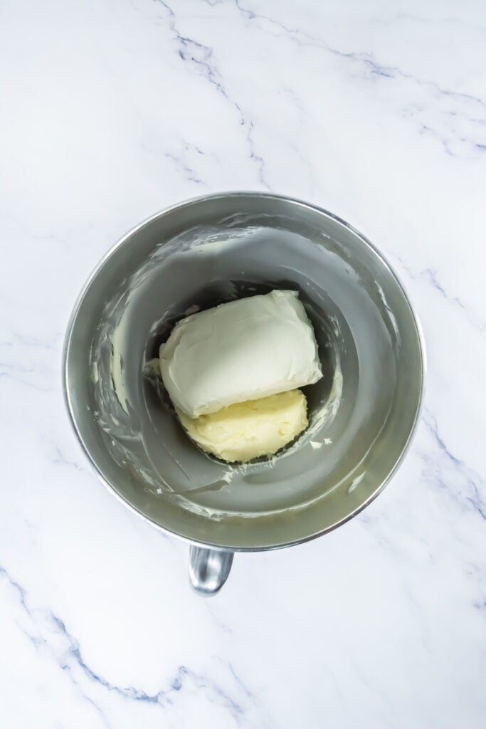 A metal mixing bowl containing a block of cream cheese and a stick of butter on a white marble surface, ready to be blended into the perfect filling for Pumpkin Spice Whoopie Treats.