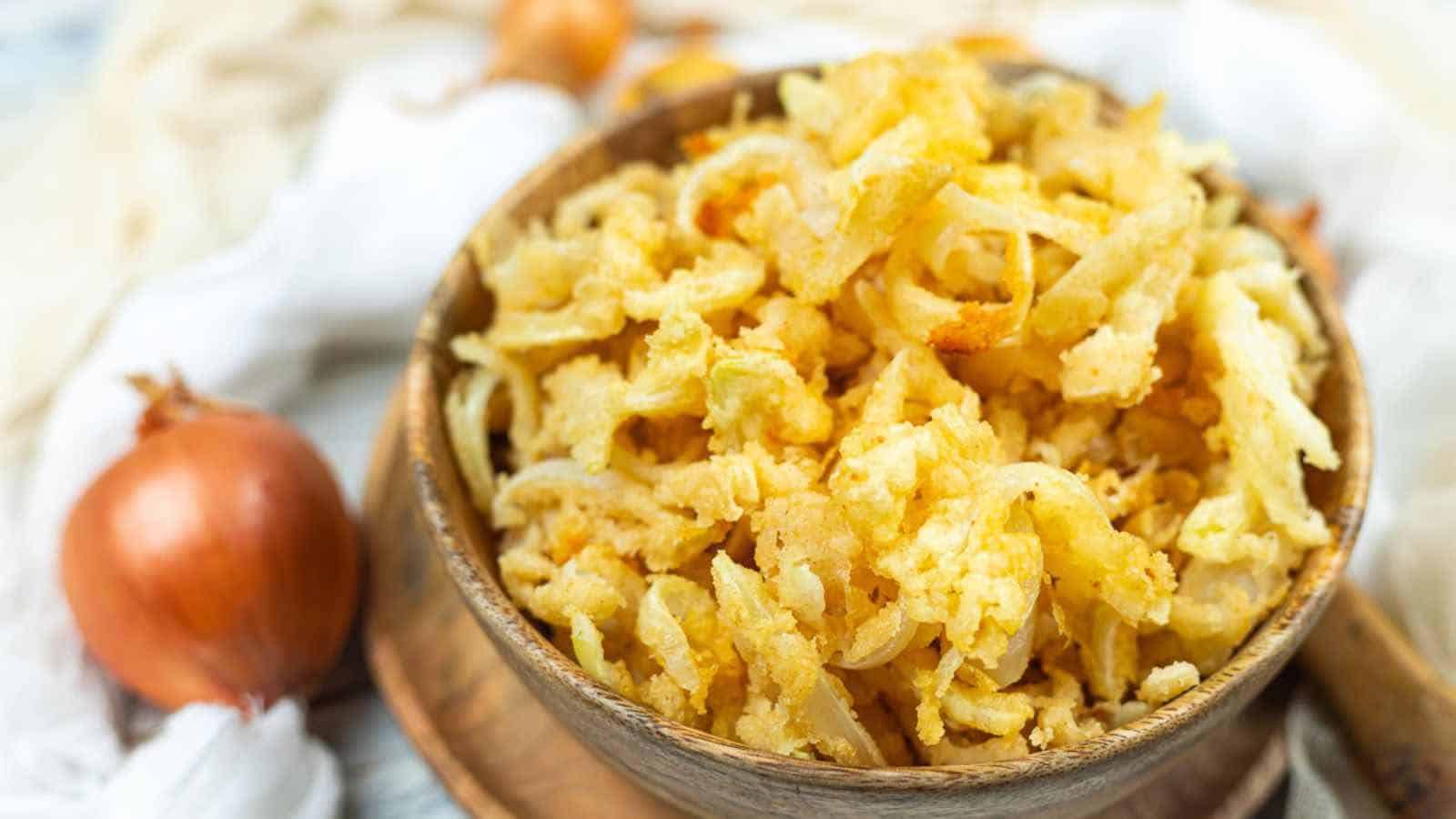 A wooden bowl filled with crispy fried onions, placed on a wooden tray.
