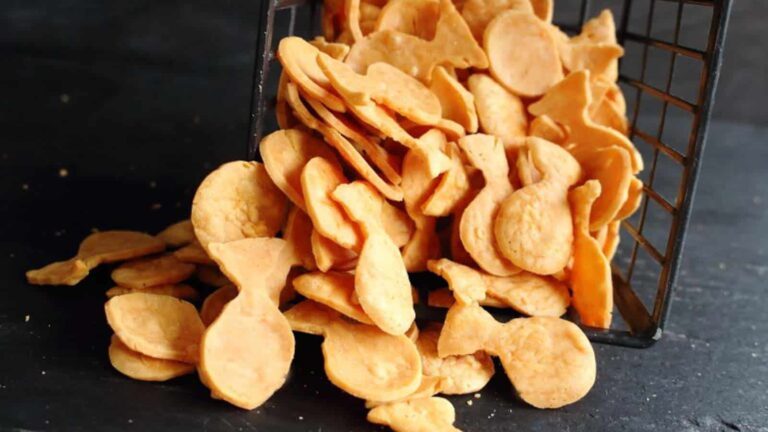 A wire basket tipped over, spilling out golden, fish-shaped crackers onto a dark surface.