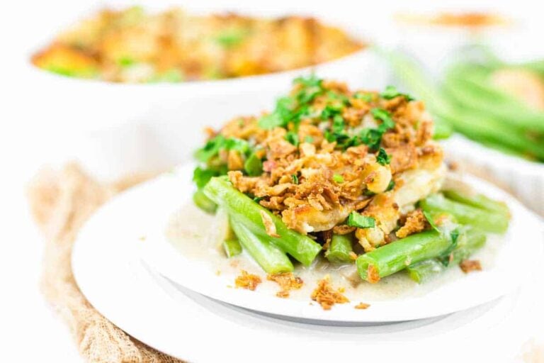 A serving of green bean casserole topped with crispy fried onions and chopped herbs on a white plate.