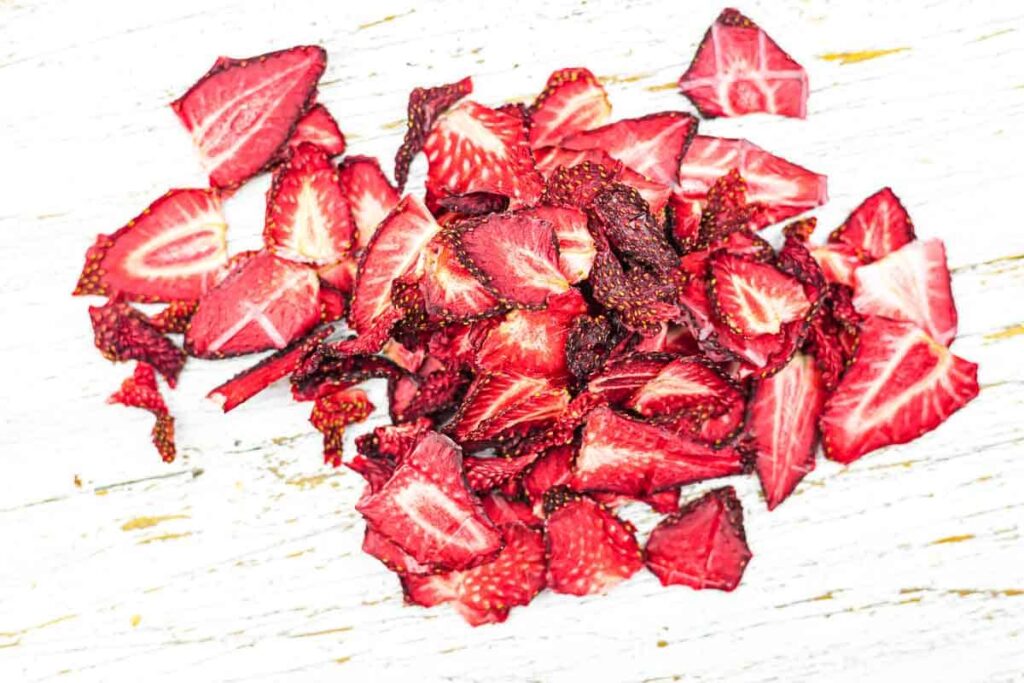 A pile of dried, sliced strawberries is spread on a white wooden surface.