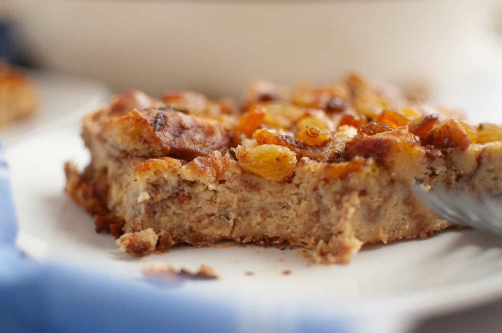 A close-up of a slice of bread pudding topped with raisins on a white plate.