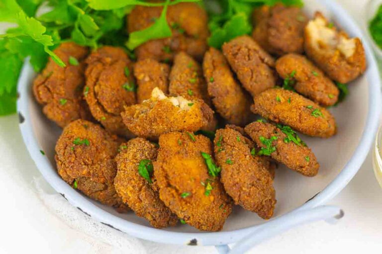 A plate of crispy, golden-brown fried patties garnished with chopped parsley, with fresh greens in the background.