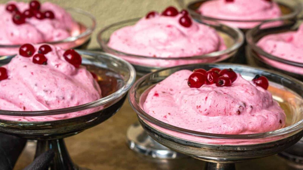 Several glass bowls filled with pink berry mousse, each garnished with a few whole red berries on top.