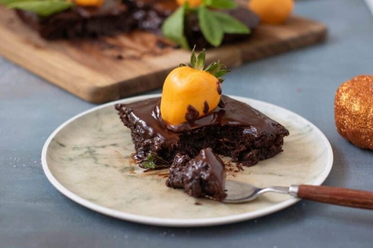 A piece of Pumpkin Patch Brownie Cake. sits on a plate with a fork. More cake is visible in the background on a wooden board.