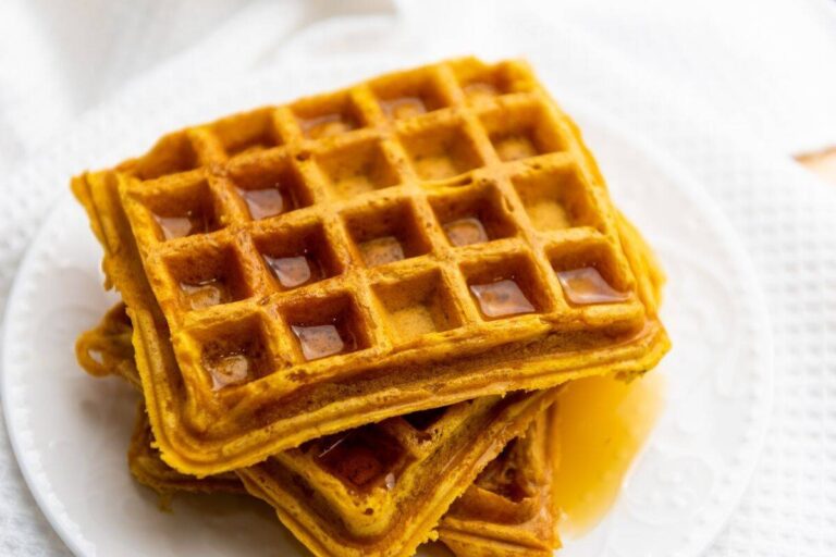 A stack of three square waffles with syrup on top, served on a white plate.