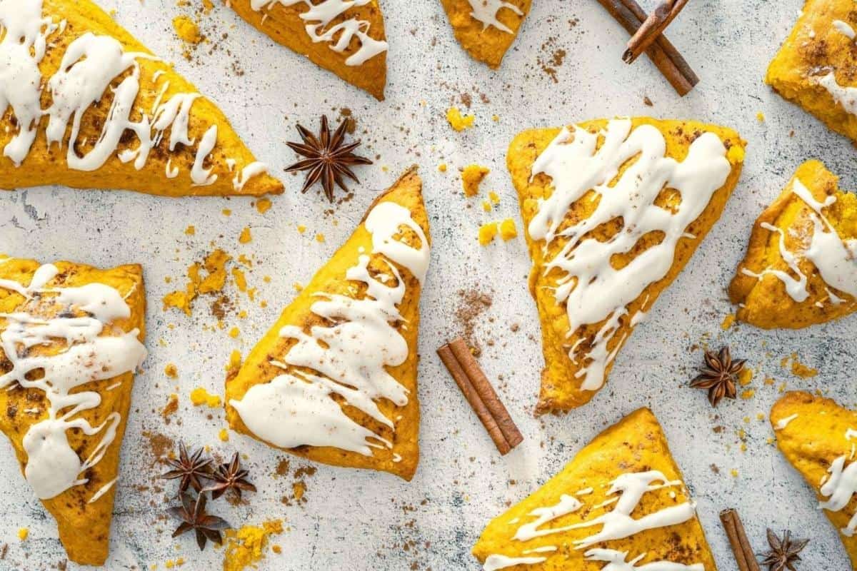 Pumpkin Spice Scones with Vanilla Glaze are arranged on a light surface, surrounded by cinnamon sticks and star anise.