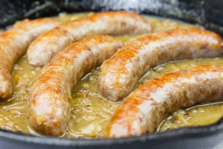 Five browned sausages simmering in a skillet with onion gravy.