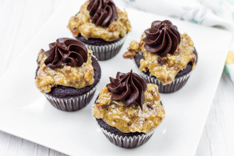 Four chocolate cupcakes topped with German chocolate coconut-pecan frosting and a swirl of chocolate icing, arranged on a white square plate.