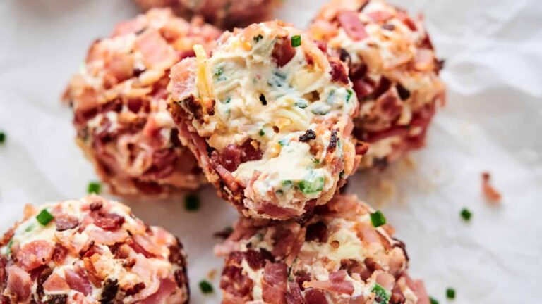 Close-up of bacon-coated cheese balls mixed with herbs and chives, arranged on a sheet of white parchment paper.