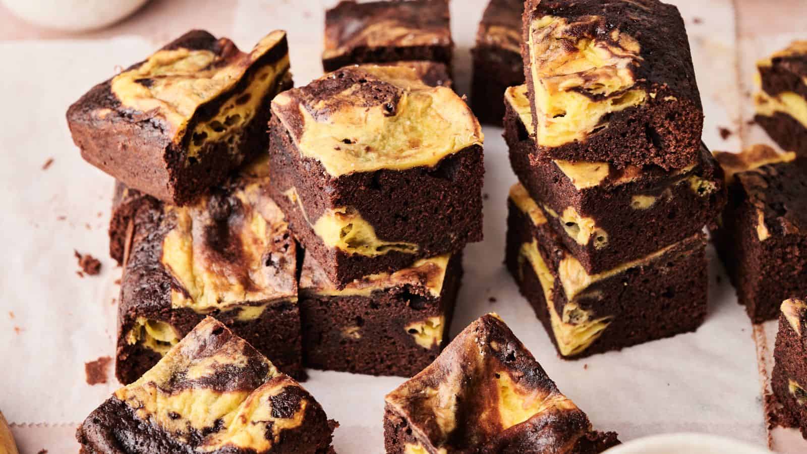 Several squares of chocolate brownies with a yellow and brown marbled pattern are stacked and arranged on parchment paper.