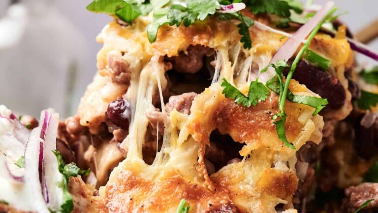 Close-up of cheesy baked nachos with beans, melted cheese, sliced red onions, and fresh cilantro on top.