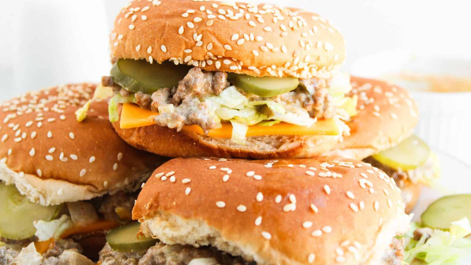 Two sesame seed burgers with cheese, shredded lettuce, ground meat, and pickles, stacked on a plate.
