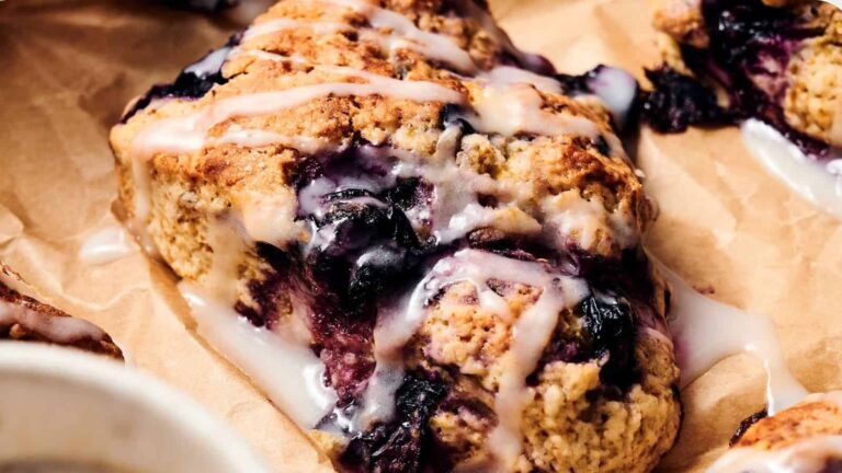 Close-up of a blueberry scone with white icing drizzled on top, placed on brown parchment paper.