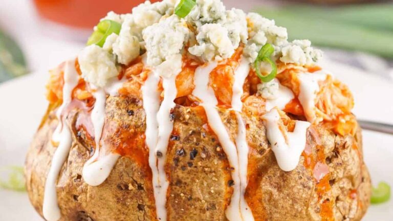 A baked potato topped with buffalo chicken, blue cheese crumbles, sliced green onions, and ranch dressing.
