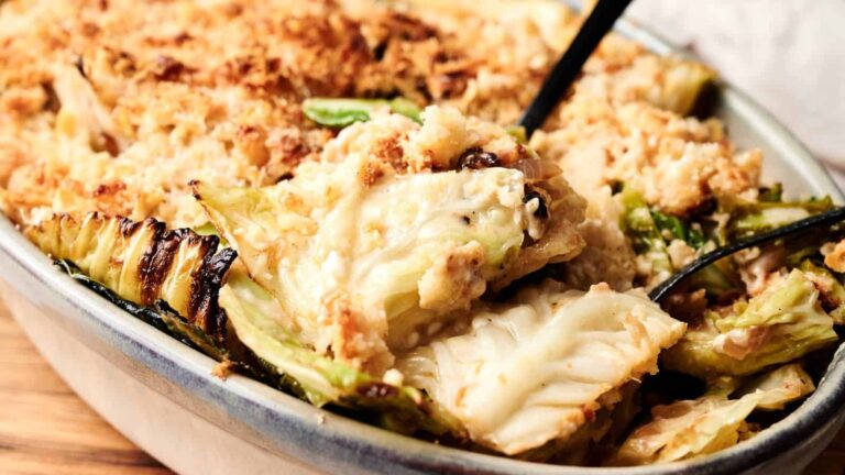 A close-up of a baked casserole dish filled with creamy cabbage gratin, topped with golden breadcrumbs, with a serving spoon scooping some out.