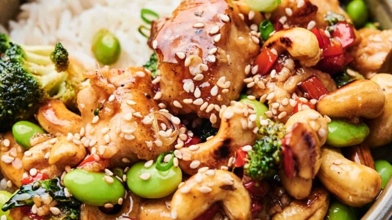 Close-up of a chicken stir-fry with broccoli, edamame, red peppers, cashews, and sesame seeds, served over white rice.