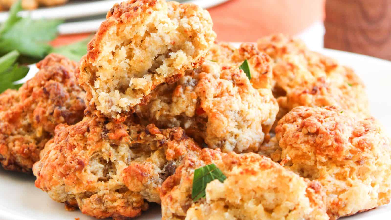 A plate of golden-brown, cheesy sausage balls stacked on top of each other, with one ball partially broken to show the inside texture.