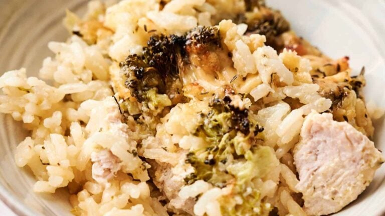 A close-up of a chicken and broccoli casserole featuring browned cheese, herbs, and green leafy garnish on top, displayed in a rectangular baking dish.