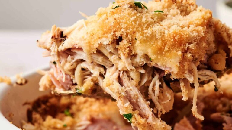 Close-up of a serving of shredded chicken casserole topped with golden breadcrumbs being lifted from a dish.