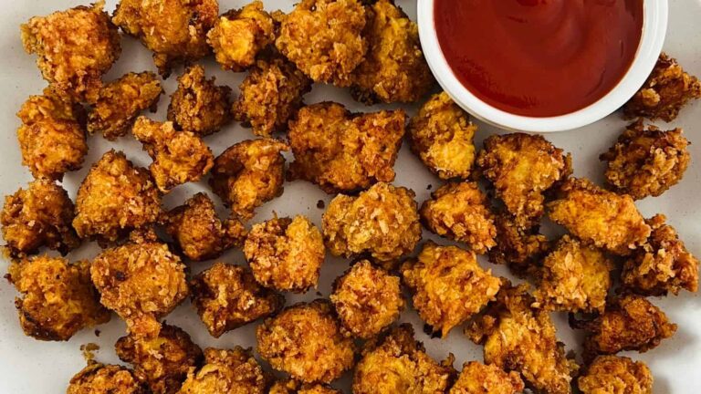 A plate of crispy, golden-brown fried cauliflower bites arranged next to a small bowl of red dipping sauce.