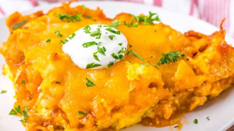 A slice of cheesy casserole topped with a dollop of sour cream and sprinkled with chopped parsley on a white plate.