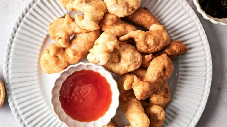A plate of golden-brown battered chicken pieces served with a small dish of orange dipping sauce.