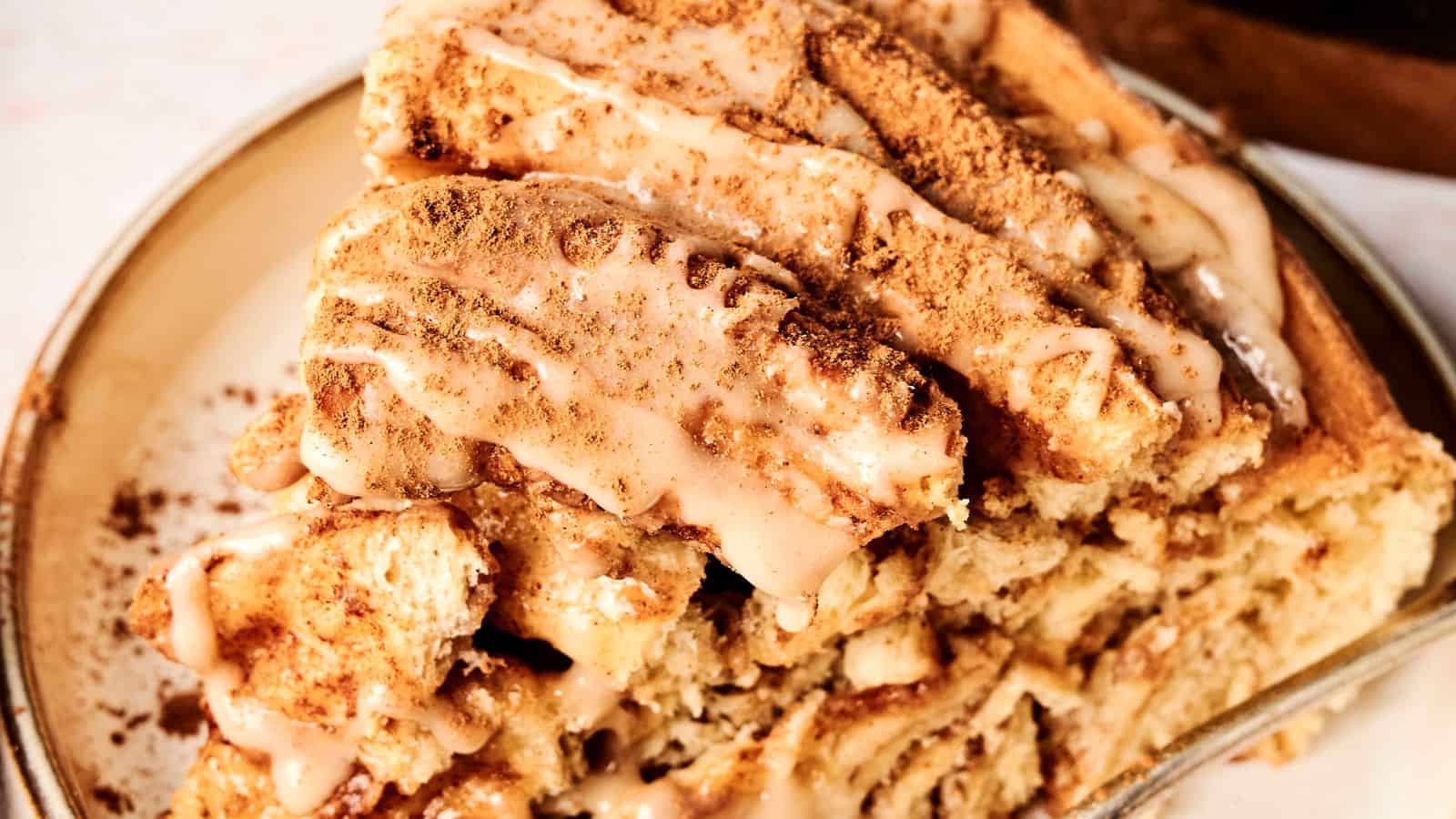 Close-up of a cinnamon roll cake slice topped with icing and sprinkled with cinnamon on a plate.
