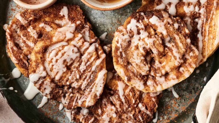Three cinnamon rolls topped with white icing are arranged on a greenish plate, viewed from above.