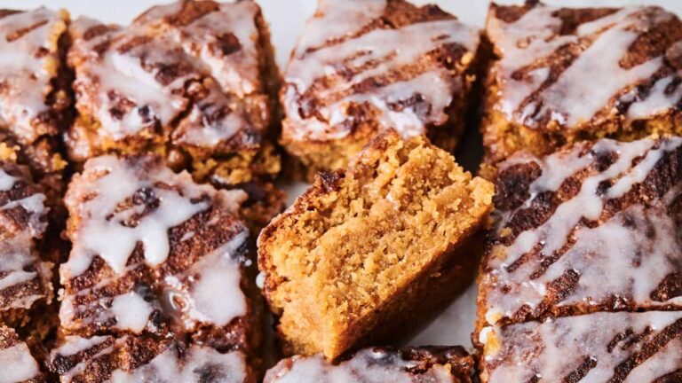 Several square pieces of moist, iced gingerbread cake are arranged closely together, with one piece turned on its side to show the interior texture.