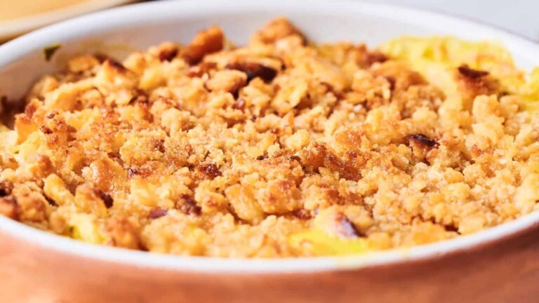A close-up of a baked casserole with a golden brown, crumbly topping in a white dish.