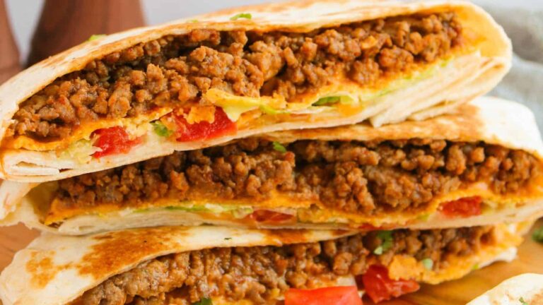 Close-up of folded tortillas filled with seasoned ground beef, diced tomatoes, lettuce, and melted cheese, cut in half and stacked.