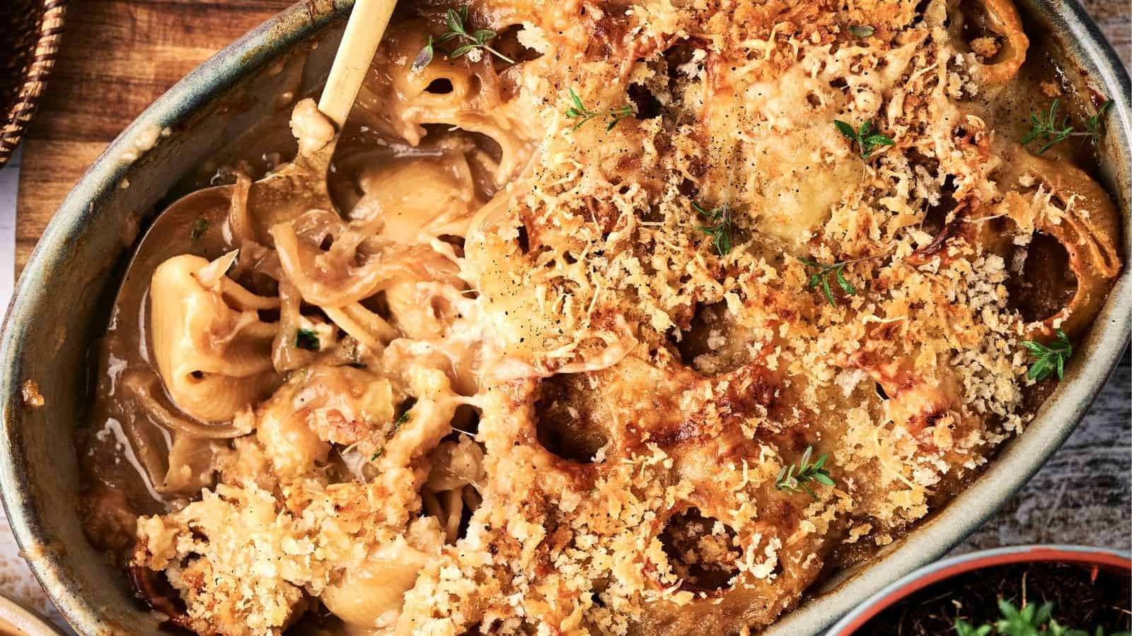 A baked casserole dish filled with creamy macaroni and cheese, topped with a golden-brown breadcrumb crust and garnished with fresh herbs.