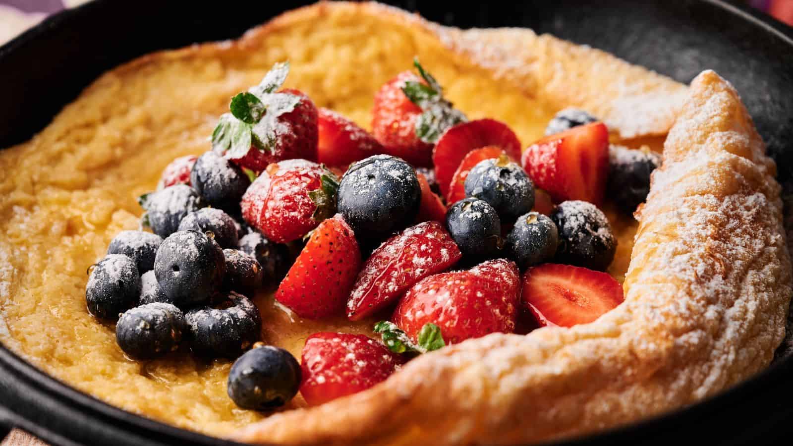A Dutch baby pancake in a skillet topped with fresh strawberries, blueberries, and powdered sugar.