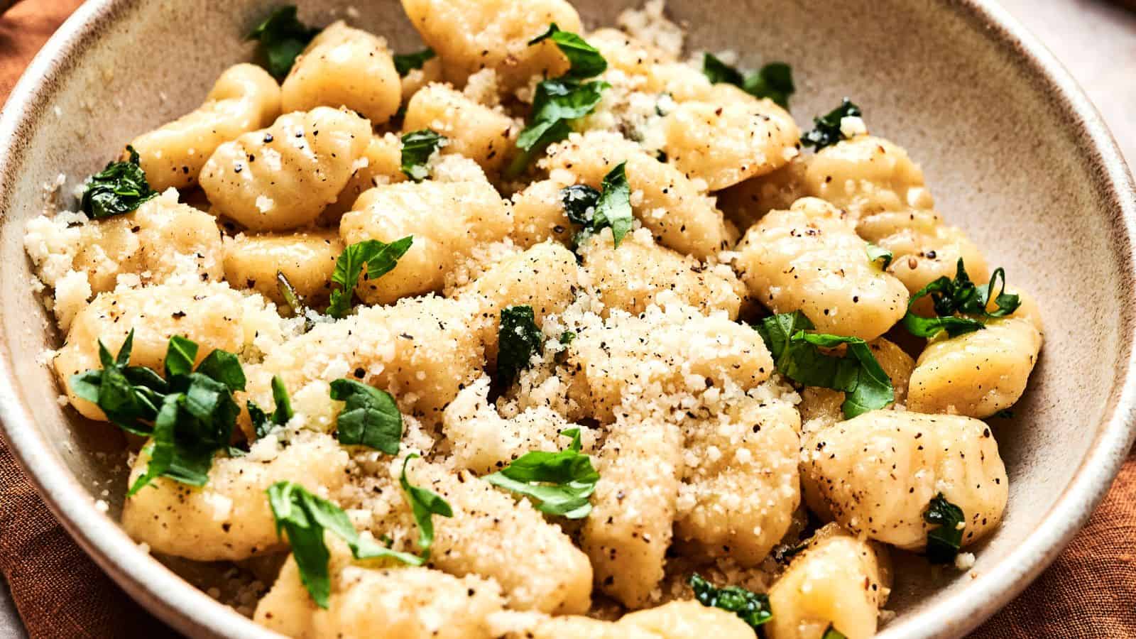 A bowl of gnocchi topped with grated cheese, fresh basil, and black pepper.