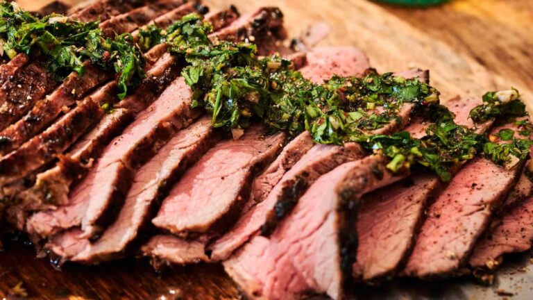 Sliced grilled steak topped with chopped fresh herbs on a wooden cutting board.