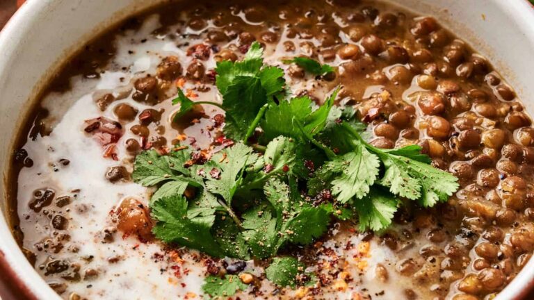 Close-up of a bowl of lentil soup topped with fresh cilantro, a swirl of cream, and a sprinkle of spices.