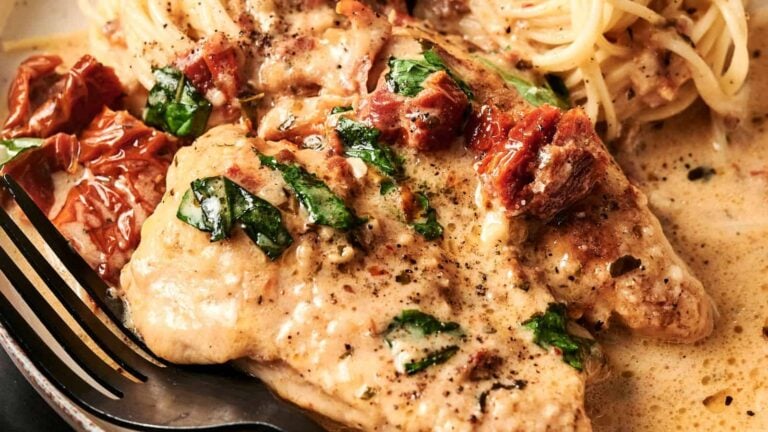 Chicken breasts in a creamy sauce with sun-dried tomatoes and spinach, served with a side of spaghetti.