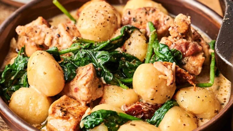 A bowl of gnocchi with pieces of chicken, wilted spinach, and a creamy sauce, garnished with cracked black pepper.