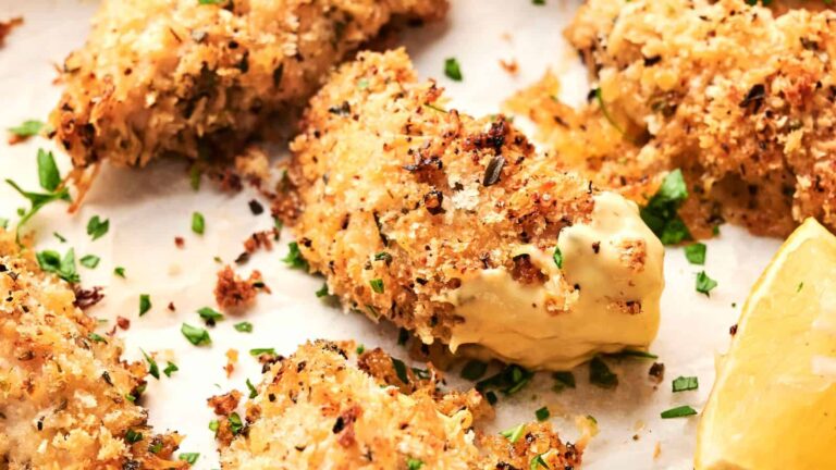 Close-up of crispy baked chicken tenders coated in breadcrumbs, garnished with chopped herbs, with a lemon wedge on the side.