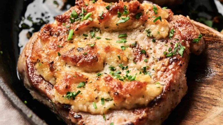A cooked pork chop topped with melted cheese and chopped herbs on a wooden spoon.