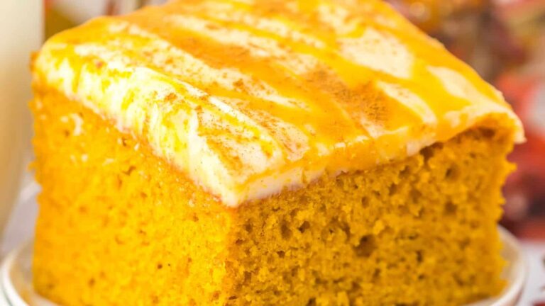 A close-up of a slice of pumpkin cake with cream cheese frosting and a drizzle of orange sauce on top.