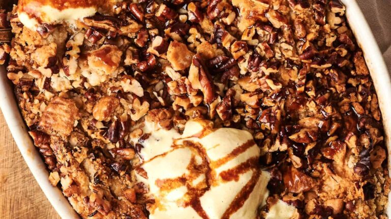 Close-up of a baked dessert topped with chopped pecans and a scoop of vanilla ice cream drizzled with caramel sauce.